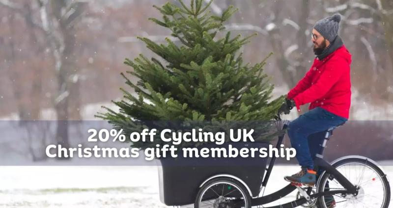 A man rides a cargo bike with a large Christmas tree in the front basket through the snow