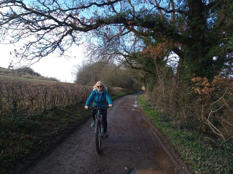 A woman is riding along a muddy country lane in winter. She is riding a mountain bike.