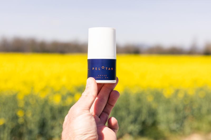 Pelotan roll on suncream being held up against a field of yellow flowers