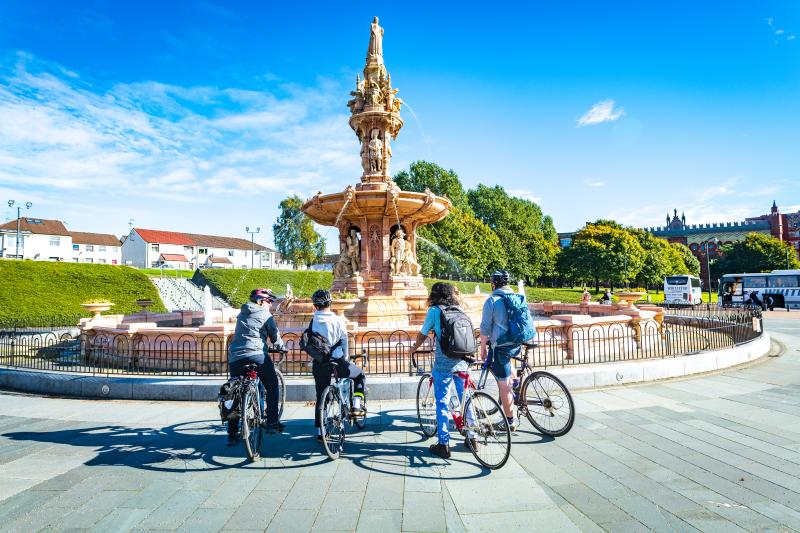 Four cyclists stand in front of fountain in Glasgow