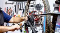 A bike is hanging on a work stand. A person is adjusting the derailleur