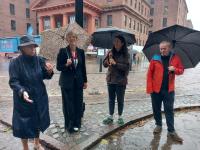 A group of four people is standing in the rain holding umbrellas in a cobbled street in Liverpool