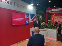 A man in a suit is giving a talk on a stage. There's a screen behind him reading Labour in government: King's speech, building a better transport system. There's another man in a suit standing in front of the stage