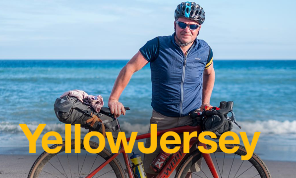 Male presenting person on the beach with a 'Yellow Jersey' logo overlaying