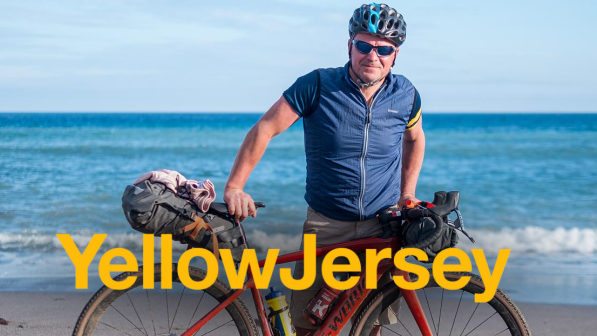 Male presenting person on the beach with a 'Yellow Jersey' logo overlaying