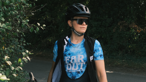 A woman in cycling clothing is standing looking away from the camera