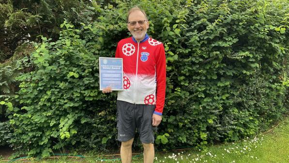 A man proudly displays a certificate in front of a green hedge  Photo by Reading CTC