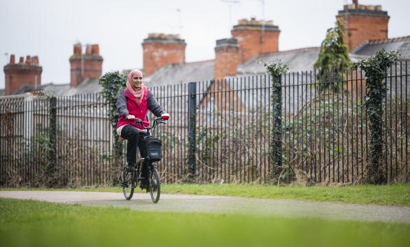 Woman smiles as she pedals electric Brompton through park.