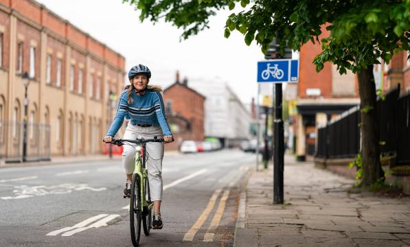 Woman wearing helmet smiles as she pedals e-cycle in cycle lane
