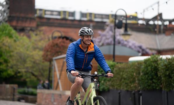 Man wearing helmet and blue jacket smiles as he pedals yellow e-cycle over bridge