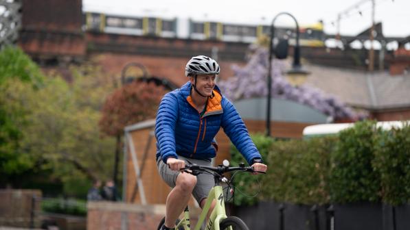 Man wearing helmet and blue jacket smiles as he pedals yellow e-cycle over bridge