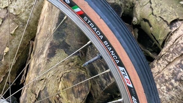 The Challenge Strada Bianca 650×46B TLR tyre on a bike wheel leaning against a pile of logs