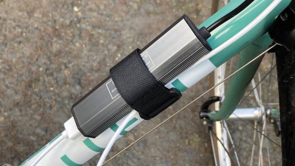 The VeloCharger Hub, a silver-grey charger attached to the down tube of a white and turquoise bike