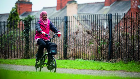 A woman in a headscarf is cycling on a paved path on an e-bike