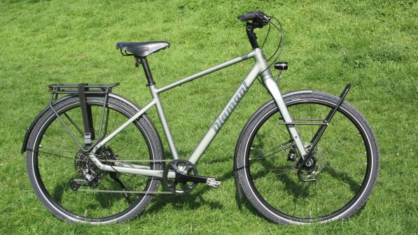 The Diamant Mahon World trekking bike, a grey bike with flat bar and front and rear rack, is propped up in a field