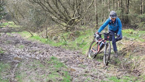 A person is pushing a loaded mountain bike through a very muddy path in the countryside