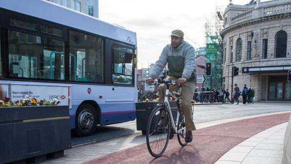 A man is cycling on separated cycle path next to a road with a bus driving alongside 
