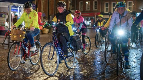 A group of women with decorated lit up bikes cycle through a town centre