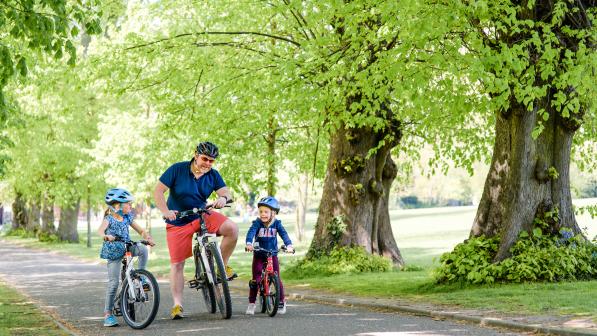 A father and two children cycling in a pleasant green space 