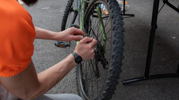 Close up of a man in an orange t-shirt sat on the ground repairing a bike wheel