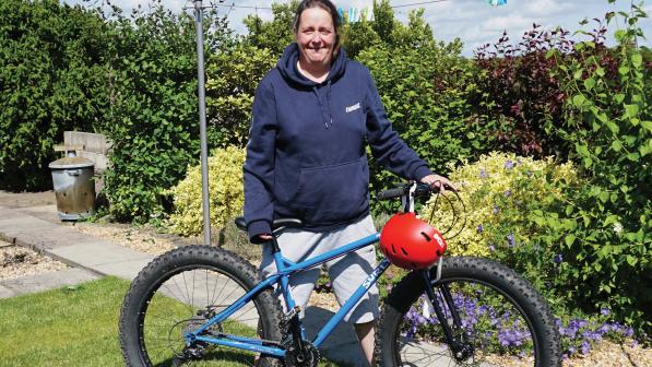 A woman is standing in a garden holding a blue fat-tyred bike with a small dog sitting in front