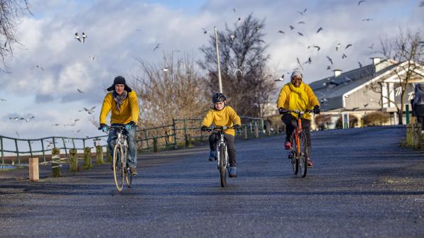 Three individuals cycling together on a road wearing yellow jumpers