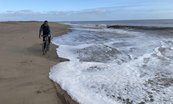 A man is cycling on the beach along the shoreline 