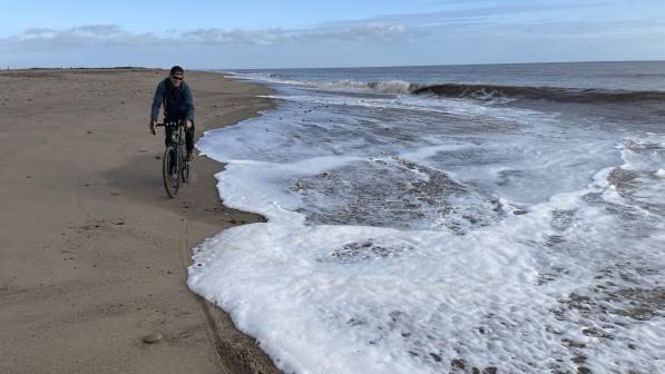 A man is cycling on the beach along the shoreline 