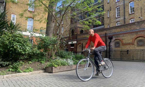 A man is cycling on a cobble path. It’s a fixie bike and he’s wearing normal clothes: a red sweater and black jeans