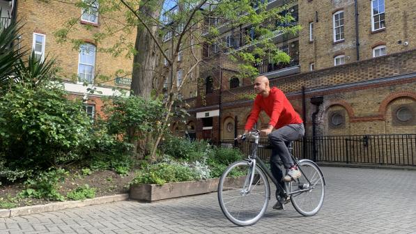 A man is cycling on a cobble path. It’s a fixie bike and he’s wearing normal clothes: a red sweater and black jeans