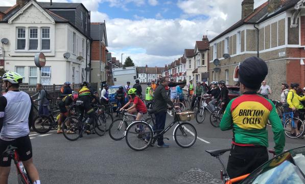 A large group of people are cycling on the road. There is a wide range of bikes and diversity of people