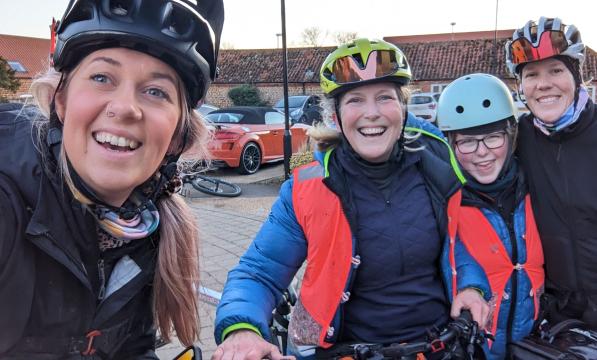 Three women pose for a selfie with a young girl. They're wearing cycle helmets