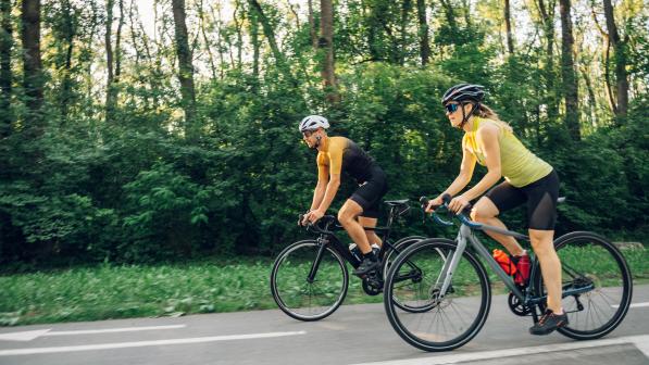 Couple riding bicycles outside of the city and wearing helmets and sunglasses