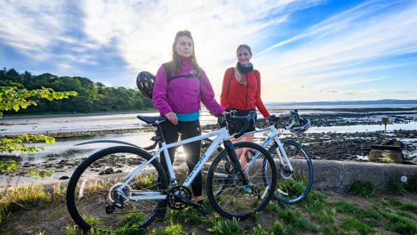 Two women standing with their bicycles by the sea.