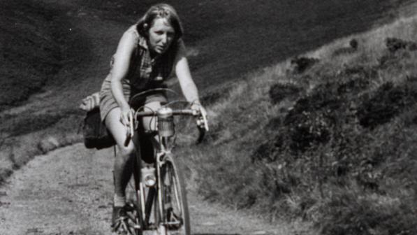 A black and white photo of a woman on a road bike cycling along a track