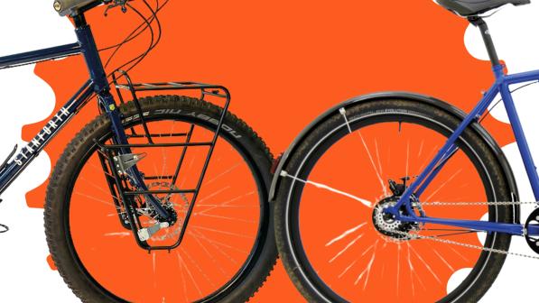 Two bikes going head to head: the Stanforth Pamira Rohloff with Gates Belt is coming in from the left, with its front wheel touching the back wheel of the Thorn Nomad Mk3 going off to the right, laid over an orange cog design