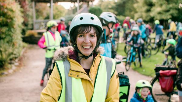 Bridie Barnett is smiling at the camera. She is wearing a white cycle helmet, a yellow jacket and yellow hi-vis vest. She is at a cycling event with loads of adults and kids with their bikes in the background.  Photo: Katie Noble