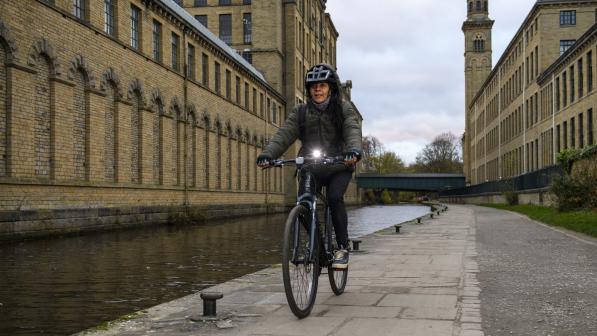 A woman is cycling along a canal tow path in the evening. She has a bright front light on her bike.