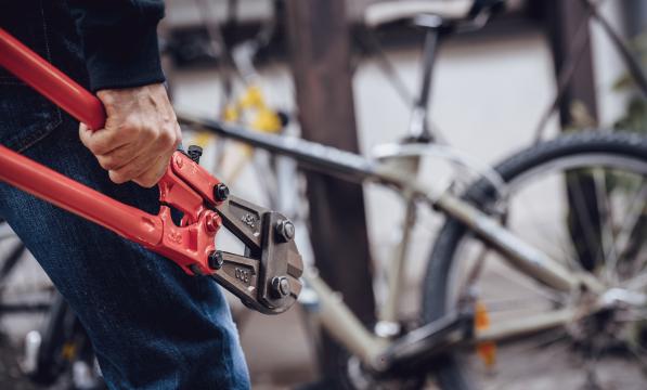 A person is carrying a heavy-duty bolt cutter towards a locked silver bike
