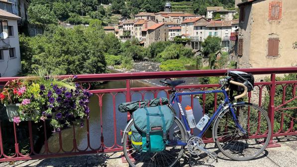 A blue touring bike is leaning against a red fence on a bridge over a stream in a town in France