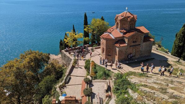 Looking down on a red brick church on a cliff top overlooking a blue sea