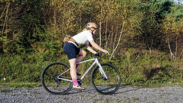 A woman is cycling on a grey Specialized gravel bike on an off-road gravel track