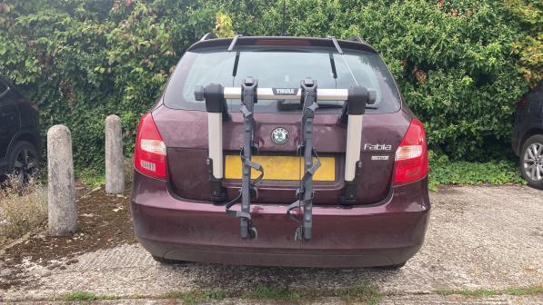 The Thule rack is fitted to the back of a purple Skoda Fabia that's parked in front of a hedge