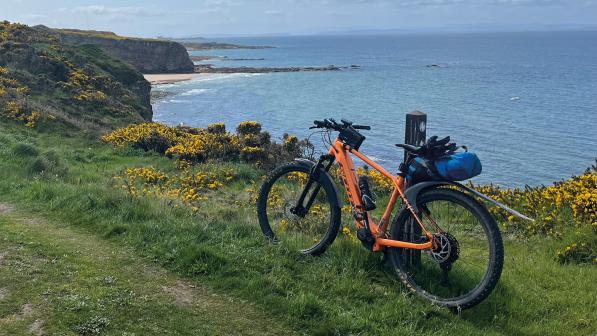 Orange ebike leaning against a pole on an offroad track with a view of the ocean behind it