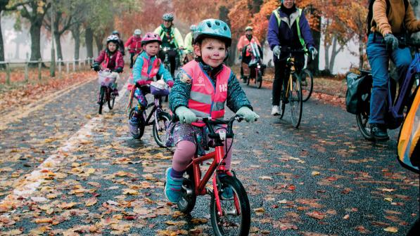 Group of cyclists including children cycling on the road, close up of a little boy on his bike wearing a helmet and high vis jacket