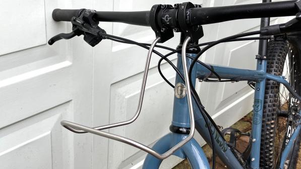 A close-up shot showing the Bagman Universal Bar Rack attached to the handlebar of a blue Genesis mountain bike