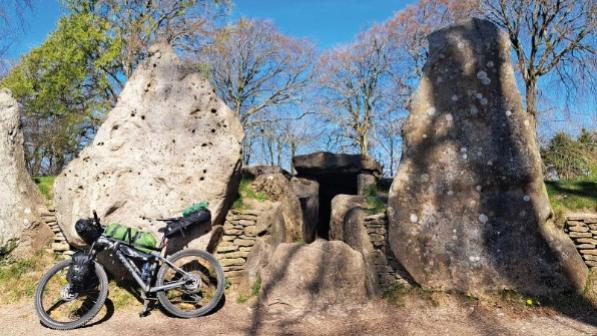 A loaded mountaing bike is leaning on a big stone that's part of a large stone barrow