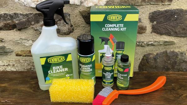 Fenwick’s Complete Cleaning Kit on a wooden shelf, comprising bike cleaning spray, chain cleaner, lube, a brush, sponge and box