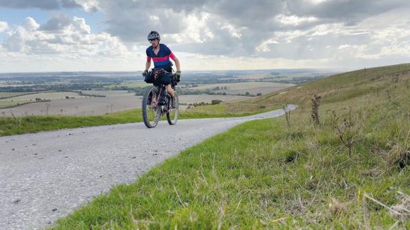 A man is riding a loaded bike along a gravel track through countryside
