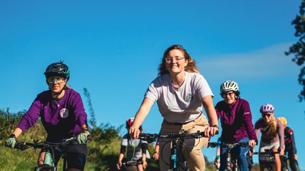 A group of women are cycling on a bright sunny day. Some are wearing helmets some are not. 